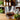 TWS Geo Whisky Glass with geometric design showcasing whisky, surrounded by greenery and blurred bottles in the background.