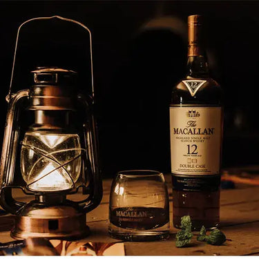 Macallan Whisky bottle and Private Collection glass beside a vintage lantern on a wooden table.