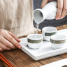 Pouring sake into cups from the 3 Pcs Vintage Ceramic Japanese Sake Set - White\Green on a wooden table.