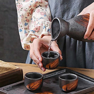 Person pouring sake into cups from a brown ceramic sake set, part of a 3 Pcs Vintage Ceramic Japanese Sake Set.