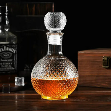 Elegant glass whiskey decanter with amber liquid, featuring a textured globe design and airtight stopper on a wooden surface.