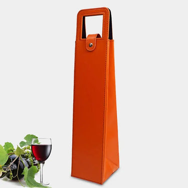 Elegant wine bottle bag in orange faux leather with a handle, next to a glass of red wine and grapes.