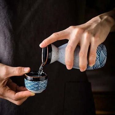 Pouring sake into cup from decanter, Japanese Waves Sake Set Ceramic, showcasing traditional Japanese artistry.