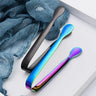 Stainless steel ice cube tongs in black and rainbow colors placed on a textured blue cloth background.