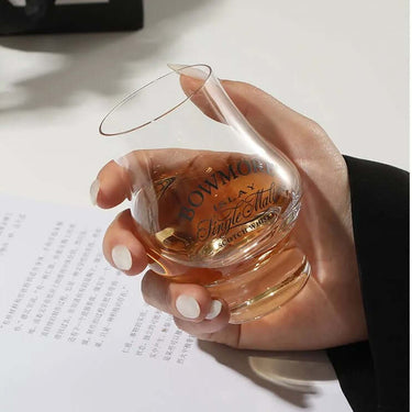 Hand holding Bowmore Single Malt Scotch Whisky Sniffer Glass filled with whiskey on a white surface